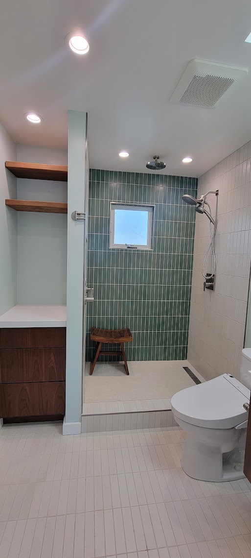 Bathroom with a green tile shower, glass enclosure, wood vanity, and an illuminated mirror