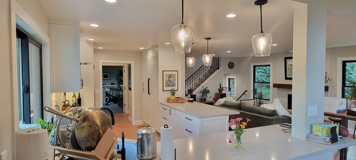 Open kitchen and living area with white cabinetry, an island, pendant lights, and wood flooring