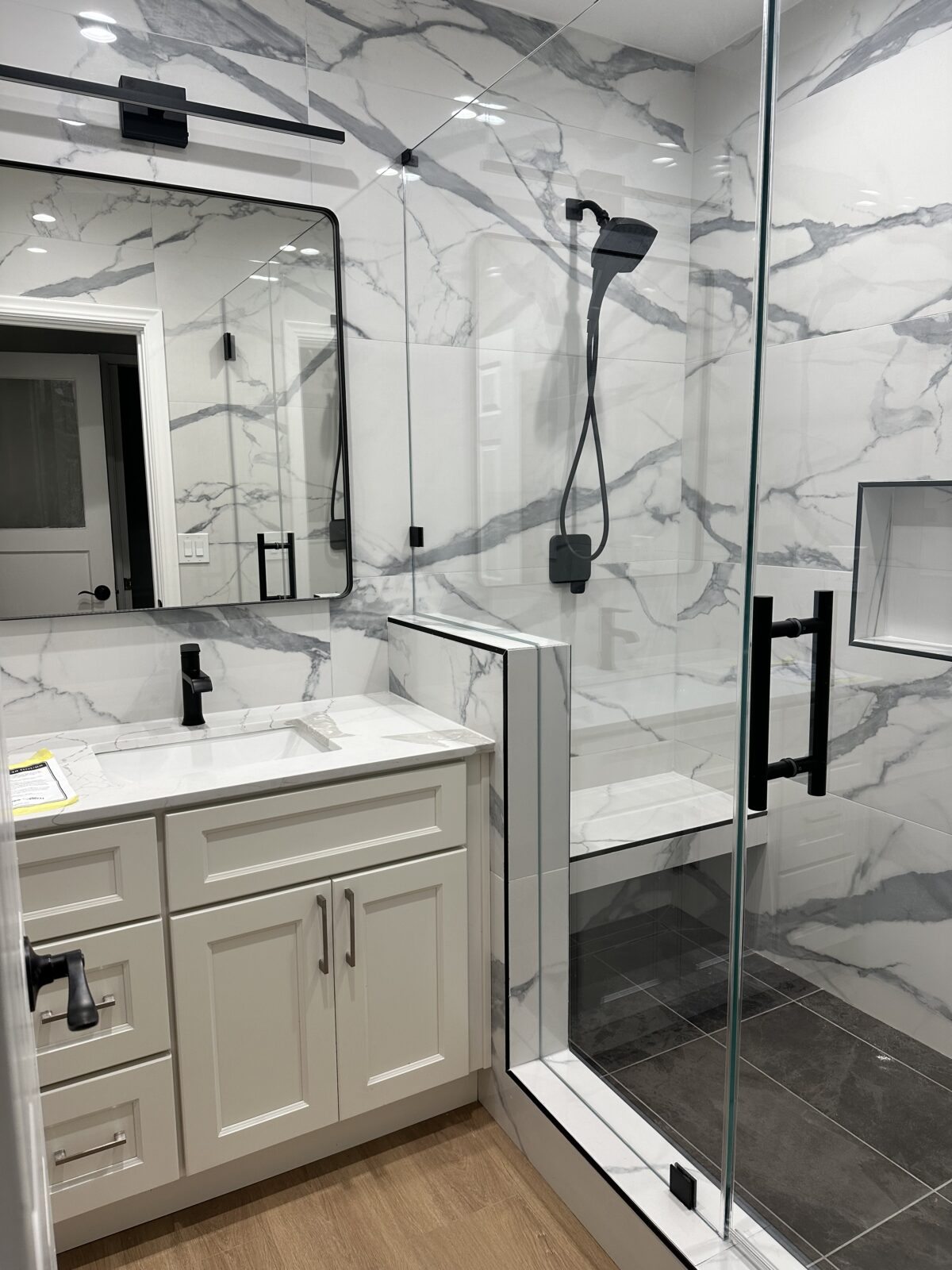 Bathroom vanity beside a marble-look tiled shower with black fixtures and a glass enclosure