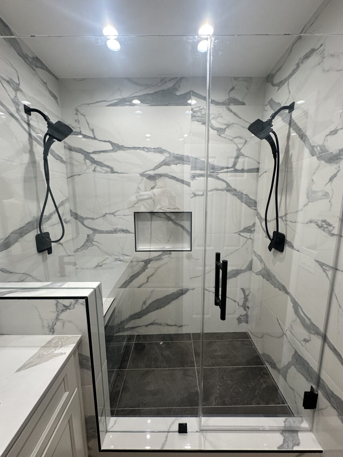 Marble-look tiled shower with black fixtures, a recessed niche, and a glass enclosure